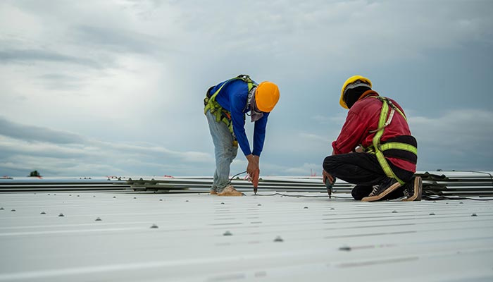 Two roofers repairing a metal roof under a stormy sky